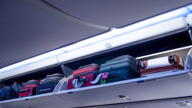 Carry On Bags Are Stuffed In An Overhead Luggage Compartment On An Airplane