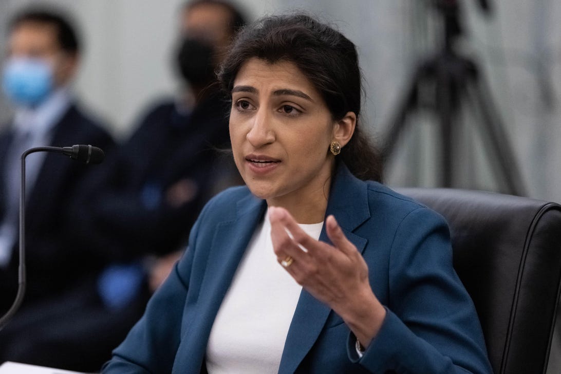 Lina Khan gestures while speaking before a small microphone at a Senate confirmation hearing.