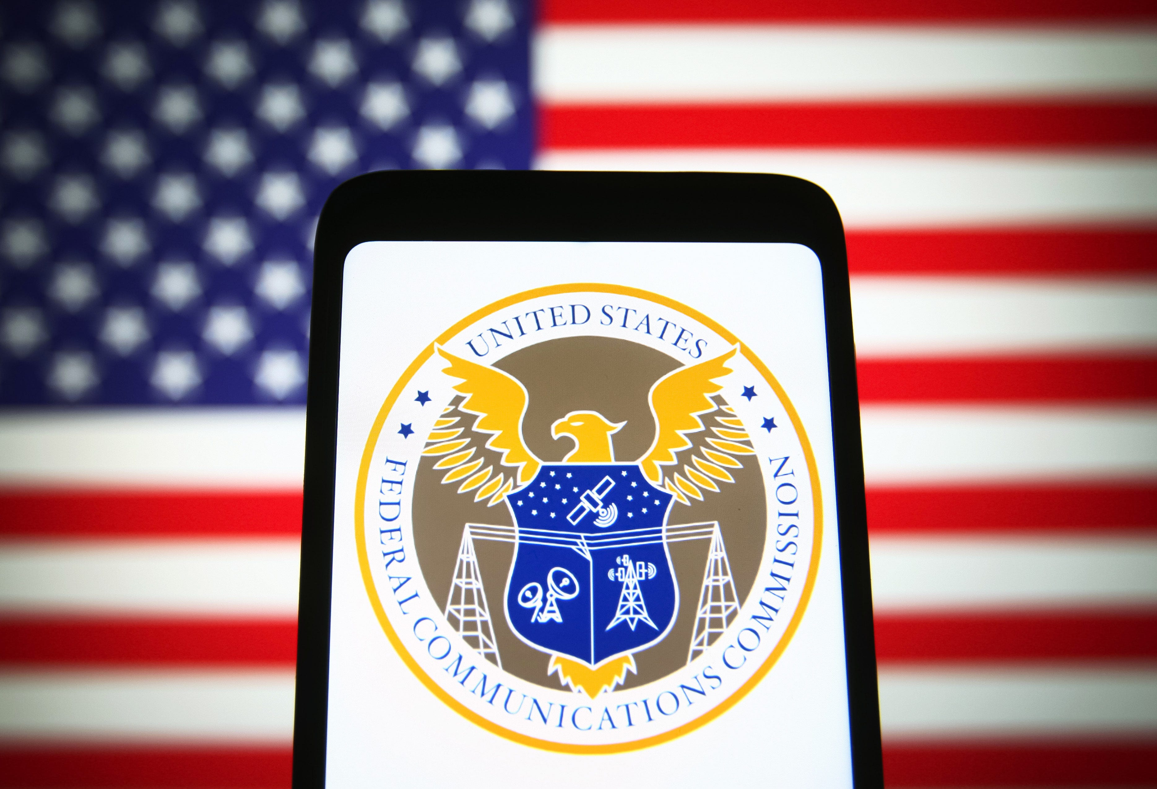 Image of phone with the FCC logo on the screen and the American Flag in the background