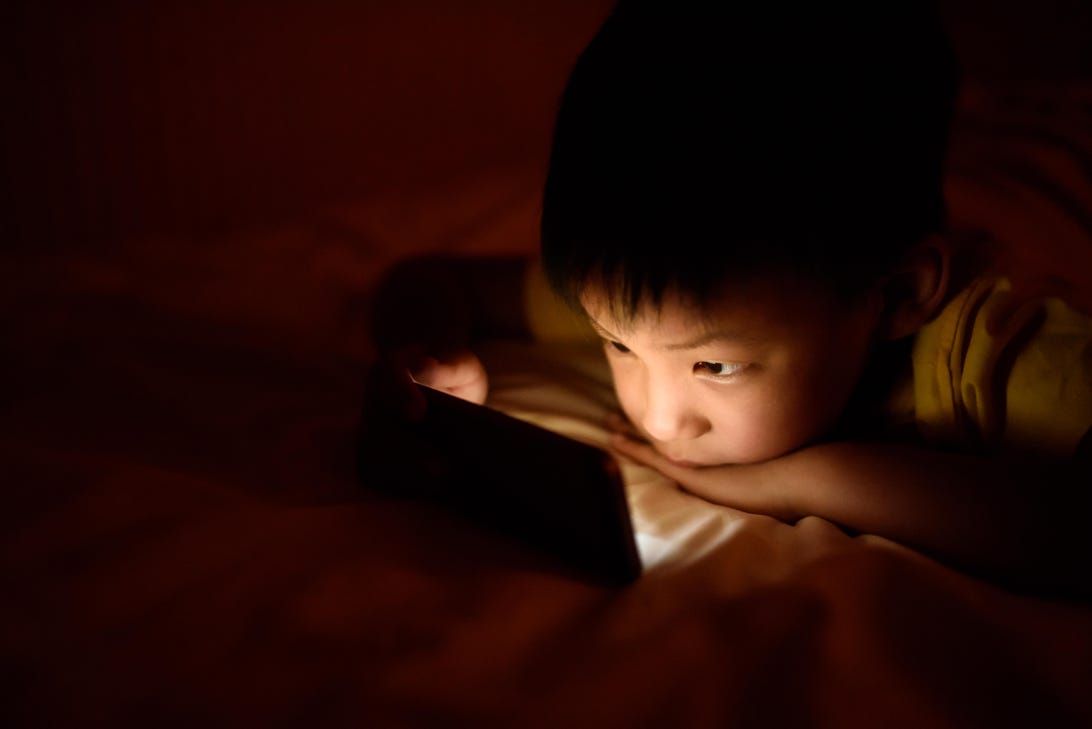 A young boy's face is illuminated by a phone screen