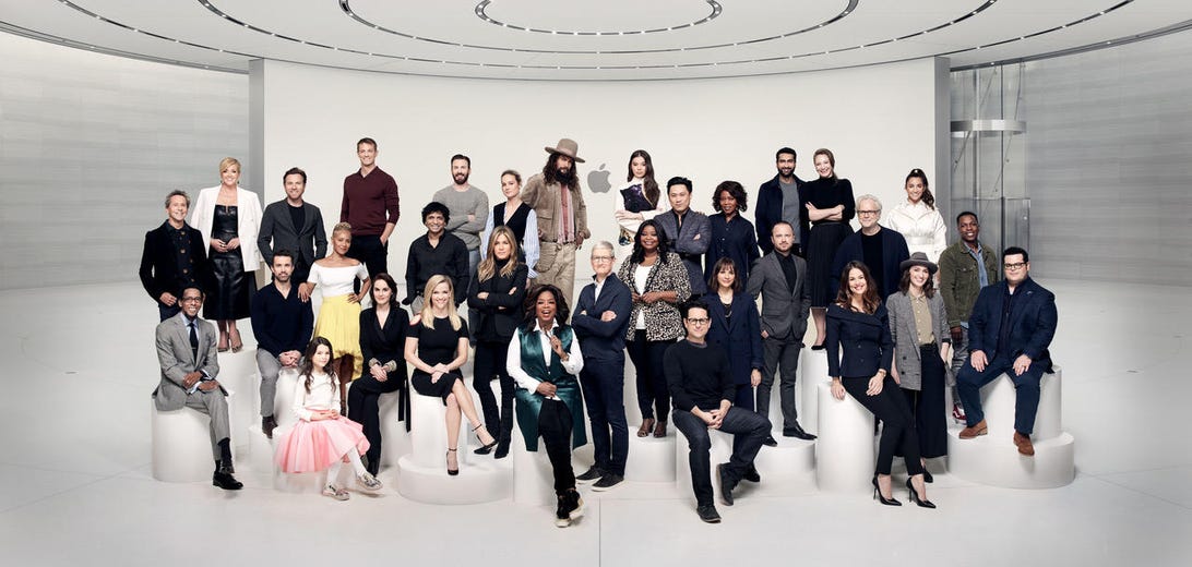A group of more than 30 stars stand in a clean white Apple lobby