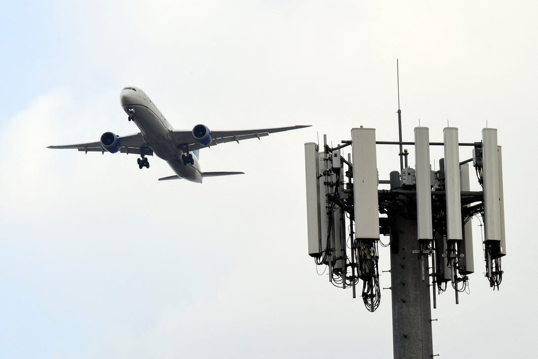 „Boeing 787“ nusileidžia Los Andželo tarptautiniame oro uoste su mobiliojo telefono bokštu pirmame plane.