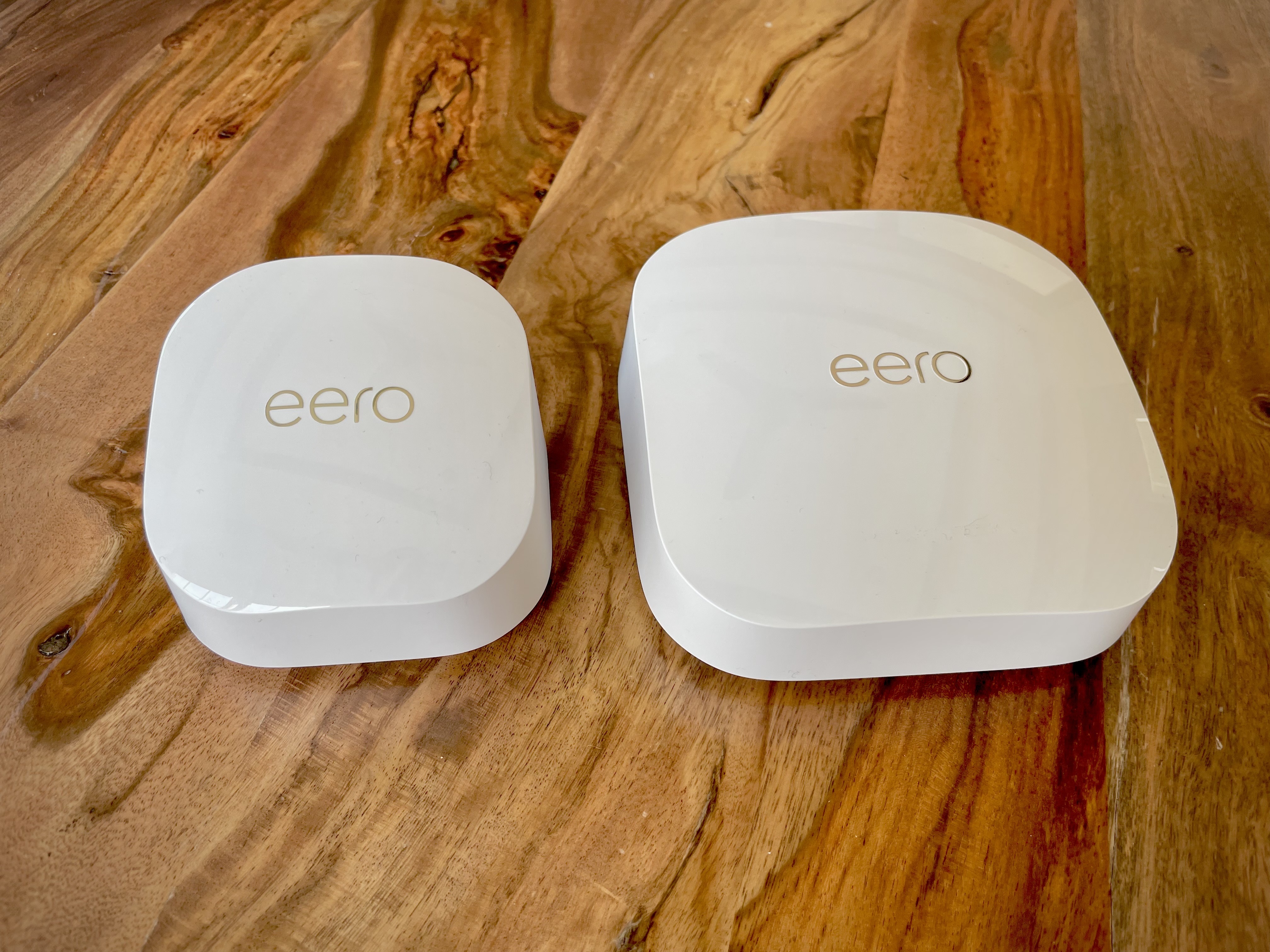 two white Eero routers next to one another on a table, one slightly bigger