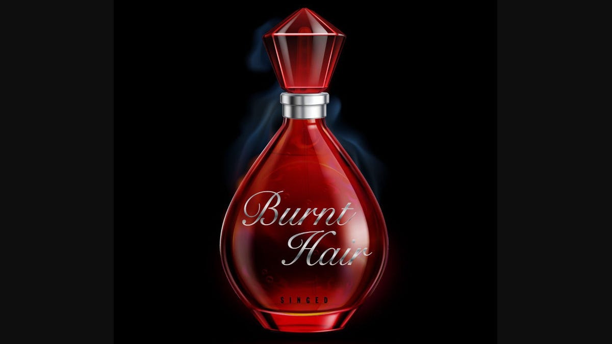A red bottle of perfume has "Burnt Hair" is silver script and the word "singed" at the bottom.