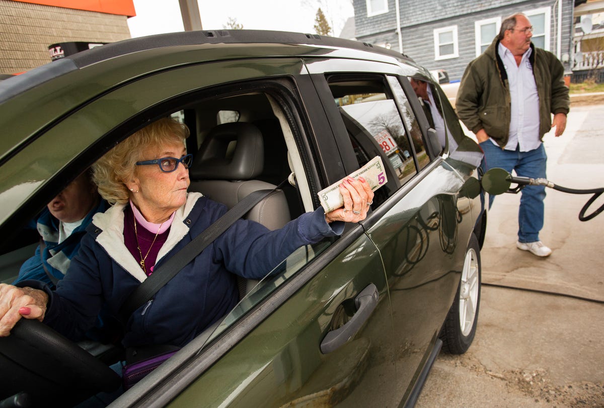 A woman in a car holds out cash to pay for gas