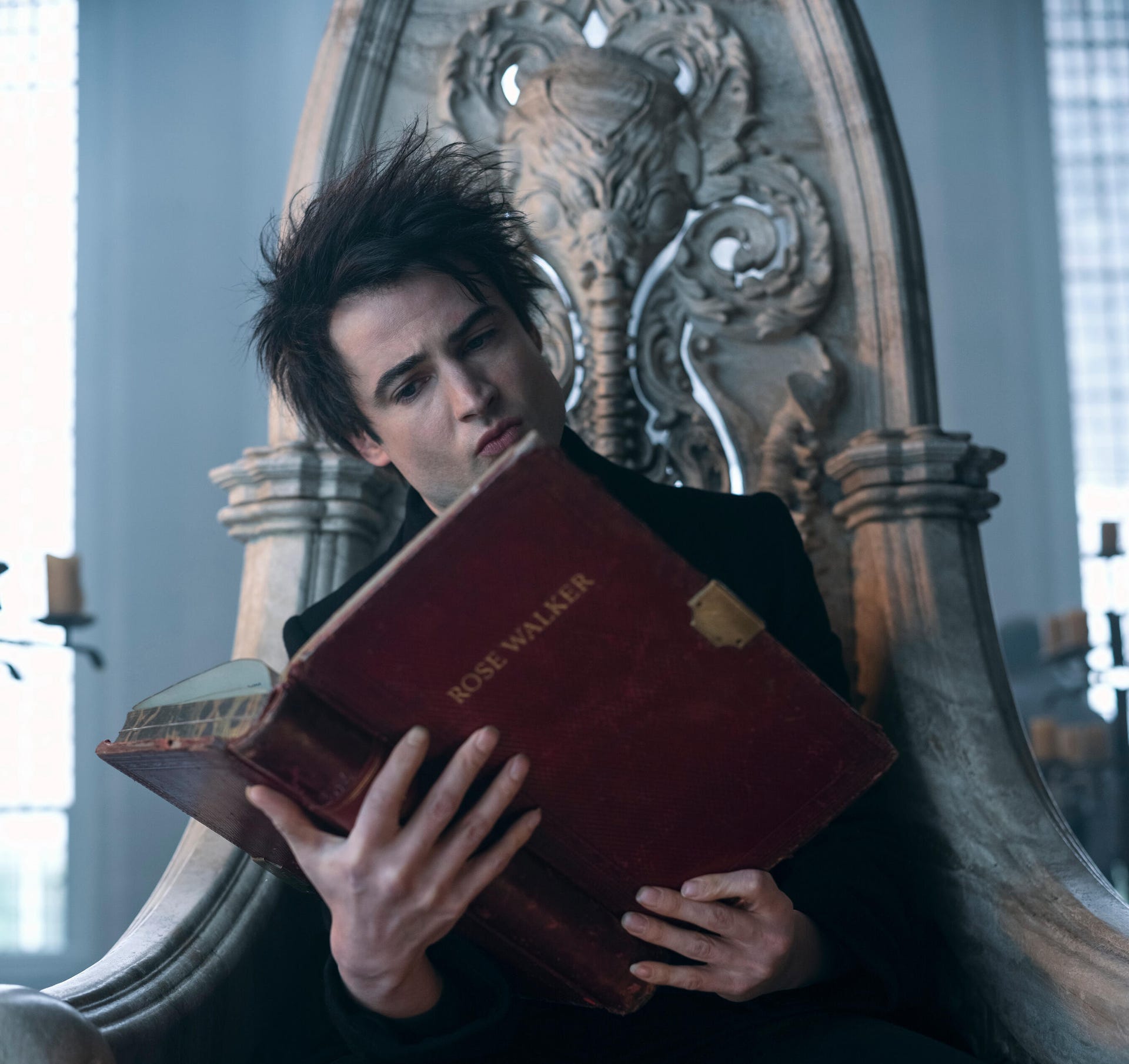 A gothic looking man sits on a throne and reads an ancient book in Netflix fantasy series The Sandman.