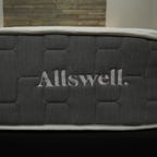 The Allswell Brick Mattress logo sitting on top of a bed frame in a well-lit room