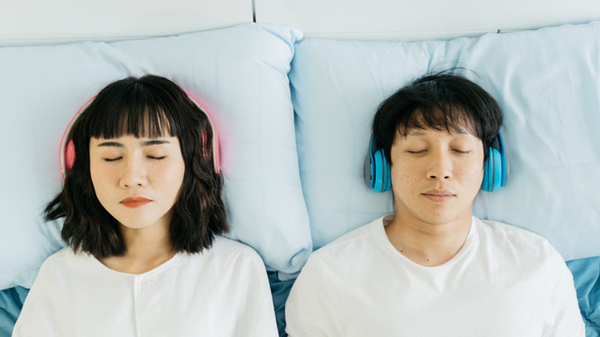 Two people in bed listening to music with headphones on.