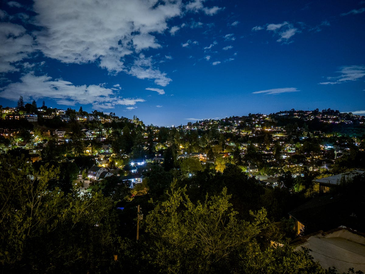 Nighttime shot of a city with dark trees, bright house lights, and a deep blue sky