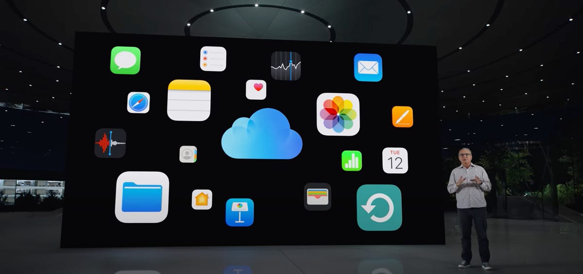 Hombre parado frente a una pantalla grande con aplicaciones de Apple sobre un fondo negro