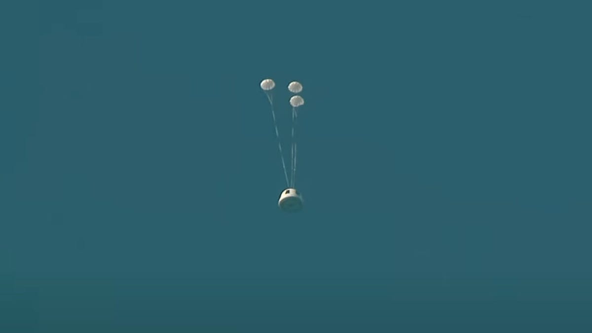 Blue Origin uncrewed capsule against a dark blue sky with three small parachutes deployed.