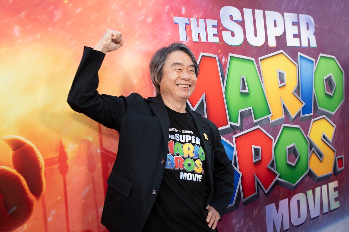 A man lifts one arm up in a Mario-style punching pose in front of a wall with the Super Mario Bros Movie logo.