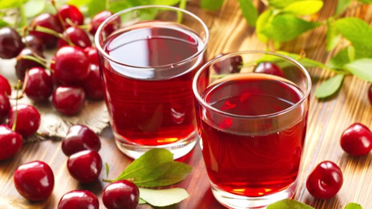 two glasses of cherry juice with cherries scattered around.