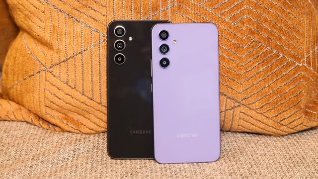 Samsung's Galaxy A54 5G in black (left) and purple (right) sitting up on a couch