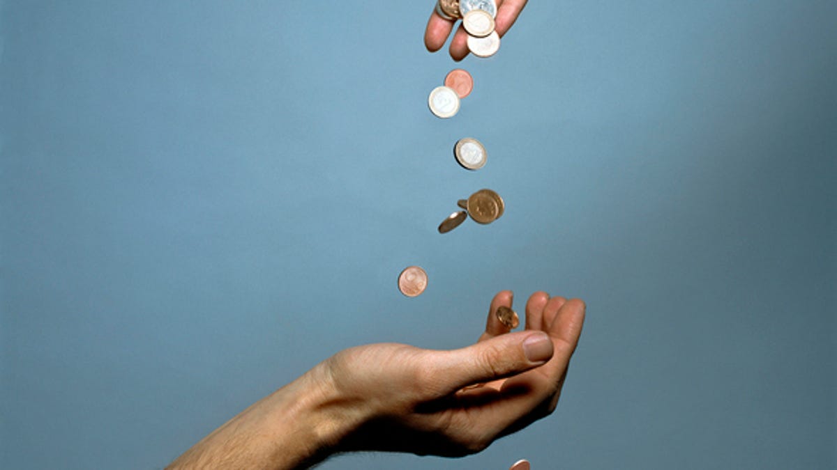 A hand drops a handful of coins above another person's open hand.