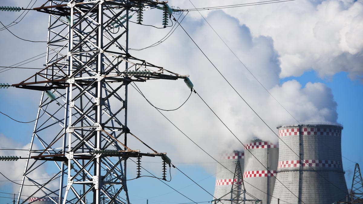Power lines and transmission towers in front of a power plants cooling tower.