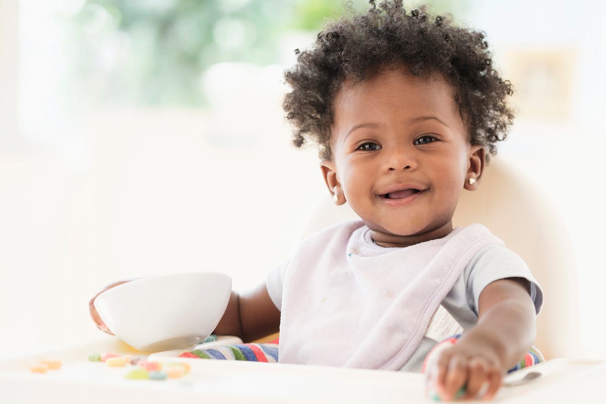 Smiling baby girl eating cereal from bowl in high chair
