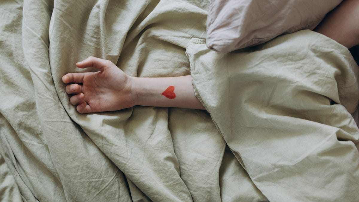 A person's arm poking out of the sheets with a heart tattoo