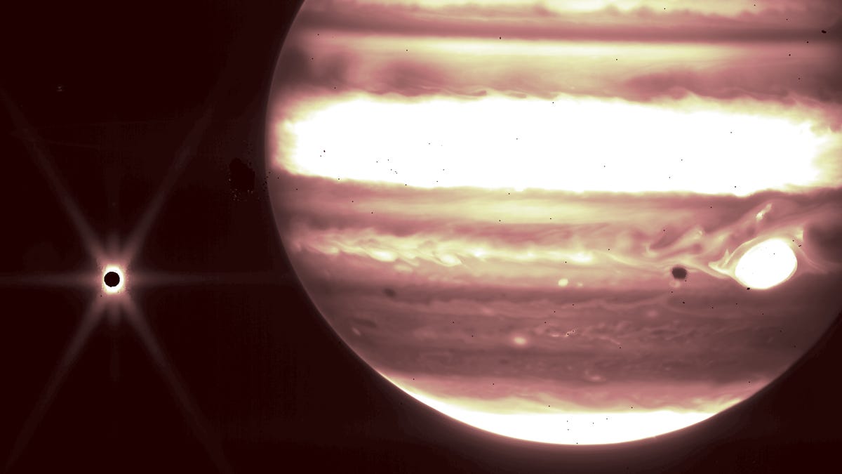An infrared view of Jupiter and its moon Europa. The infrared wavelengths see Jupiter shine brightly in yellows, browns and maroon while Europa appears as a black spot