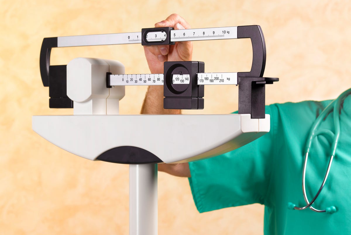 A man's arm in scrubs adjusts a weighing scale.