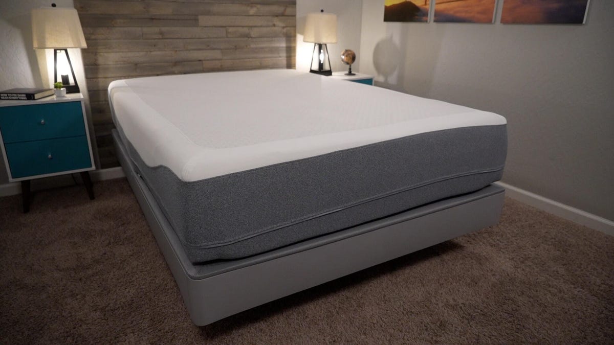 The Sleep Number Climate360 mattress and adjustable bed frame in a dimly lit bedroom with a wooden head board.
