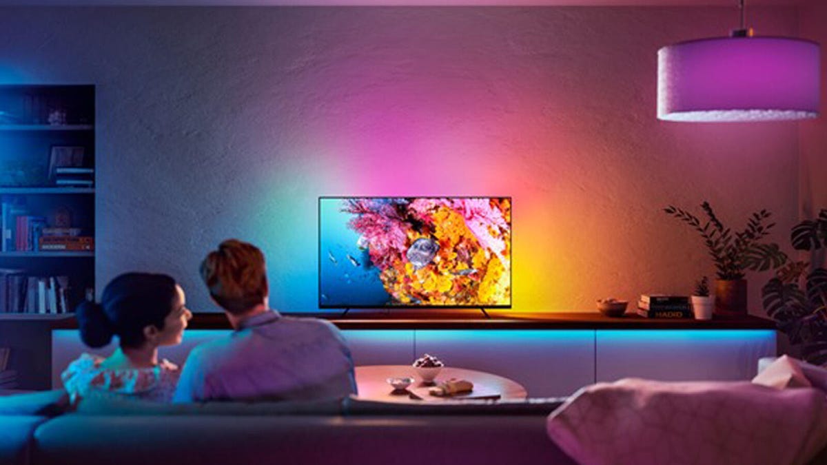 A Philips Hue Play Gradient Lightstrip lights up a TV stand and while a couple watches the TV from the couch.