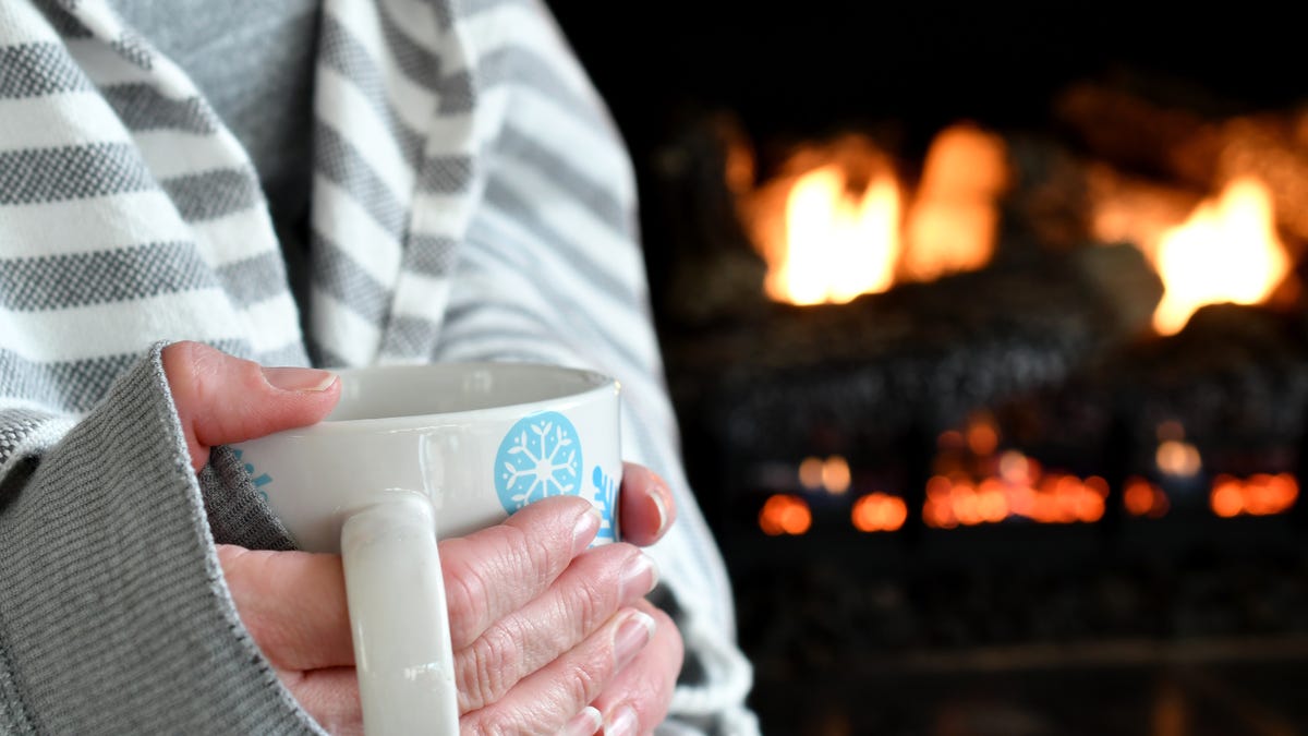 Midsection Of Woman Holding Coffee Cup By Fireplace - stock photo