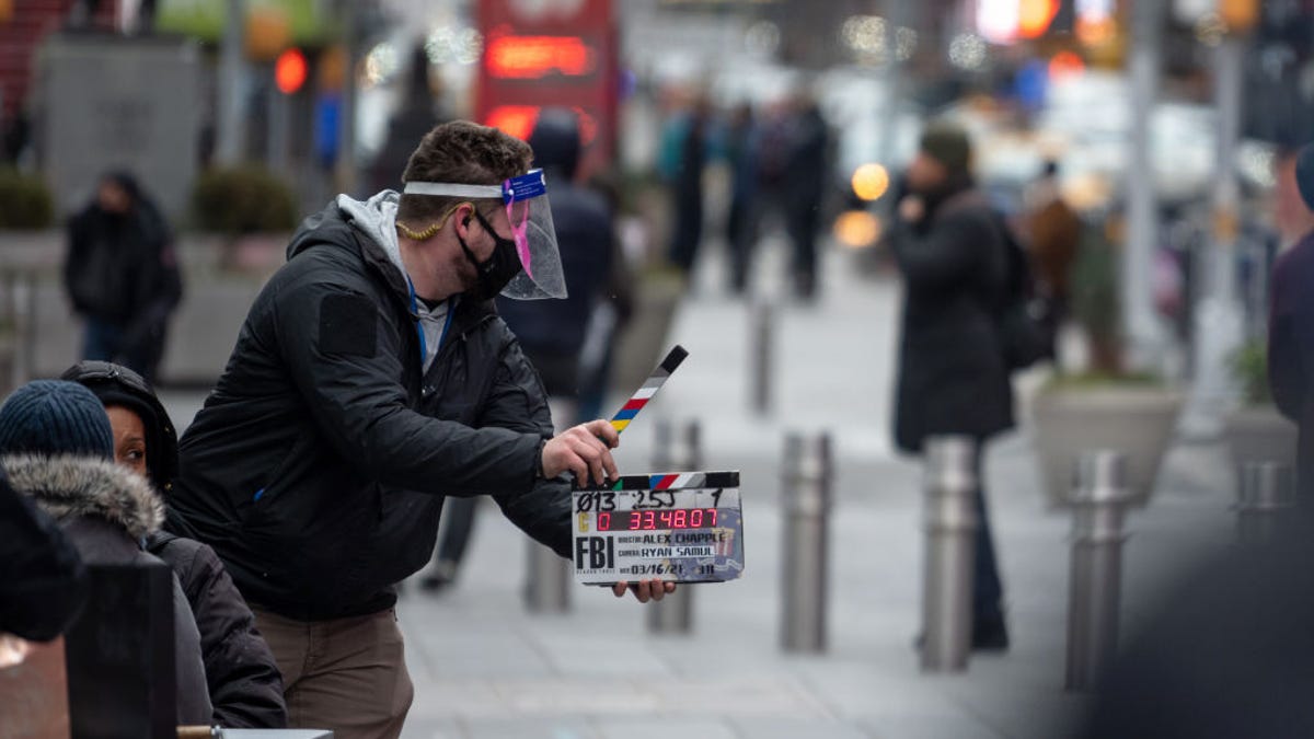 A person wearing a mask and face shield uses a clapboard during the filming of a TV series in Times Square this past March.