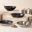 The Made In 13-piece stainless steel set is displayed on various risers and a cream-colored background.