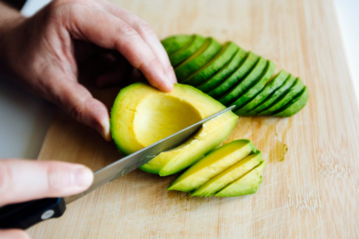 Close-up of hands with a knife cutting an avocado.
