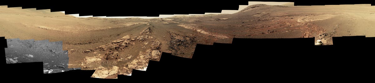 Long panorama shows Martian rocks and hills in shades of brown and red.