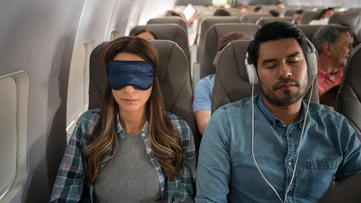 A man and a woman seated next to each other on a plane, trying to sleep.