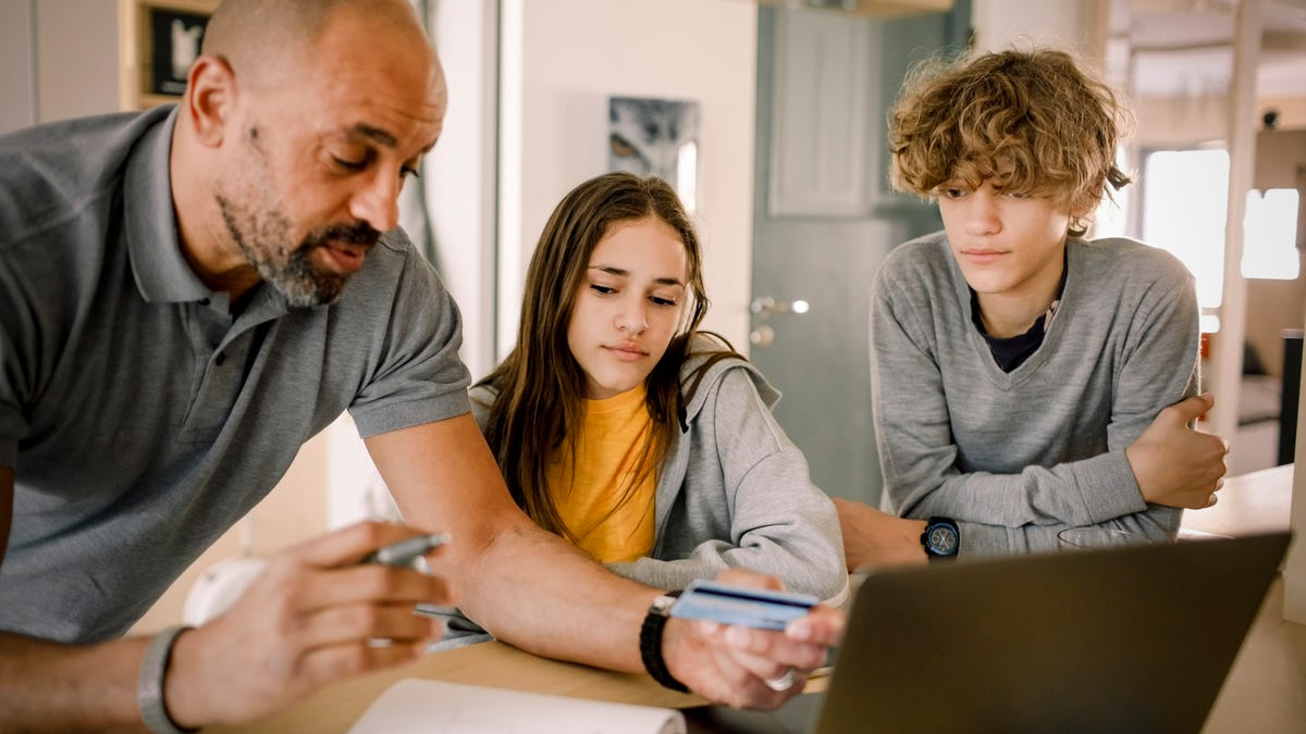 Brother and sister looking at father explaining finance with credit card at kitchen island - stock photo