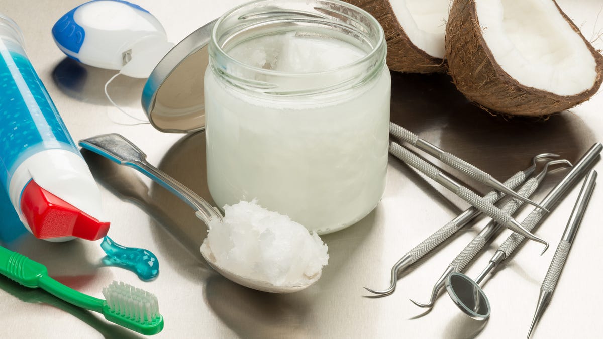 Coconut oil, halved coconut, toothbrushes and other dental tools on a table.