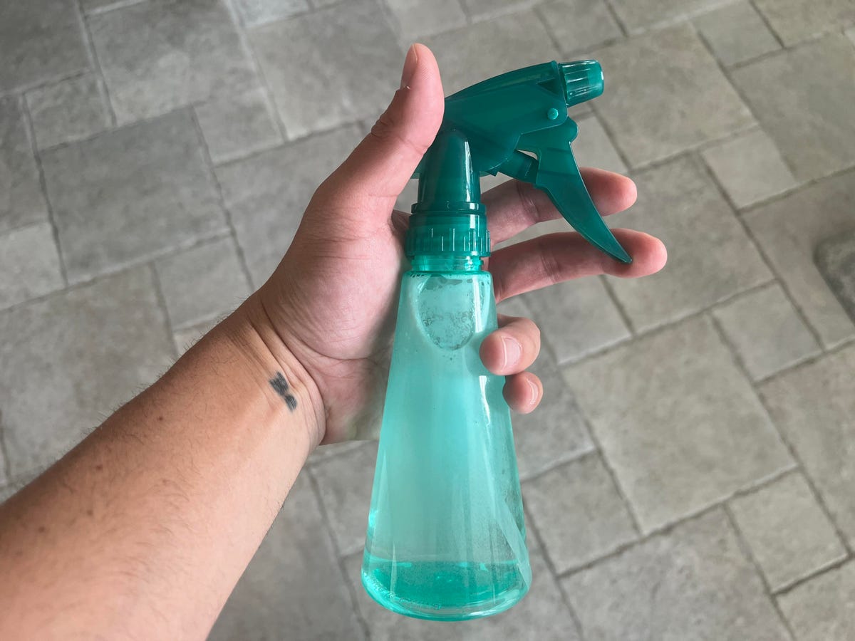 mão segurando o frasco de spray verde