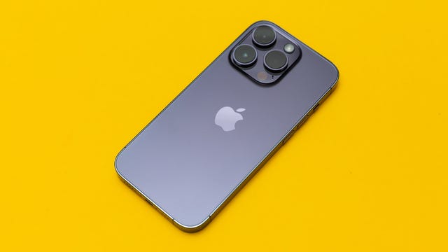 Um iPhone 14 Pro roxo escuro com três câmeras apontando para cima está sobre um fundo amarelo