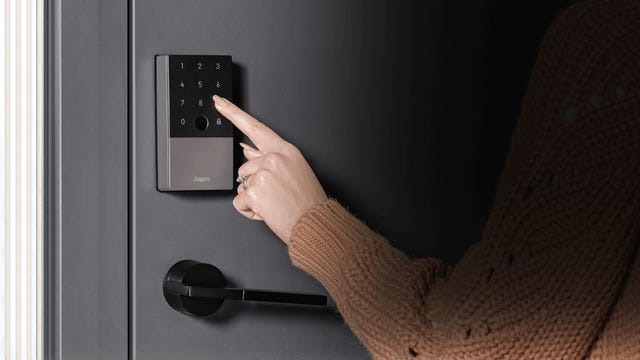 A hand touches the Aqara keypad on a gray door.