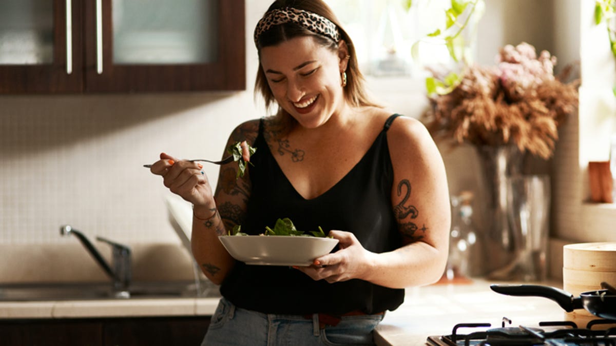 Woman leaning against her kitchen counter while she eats a salad.