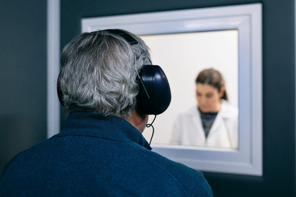 A windowed wall with a doctor on one side and a patient with headphones on the other.