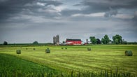A red barn in Wisconsin behind a field with hay bales.