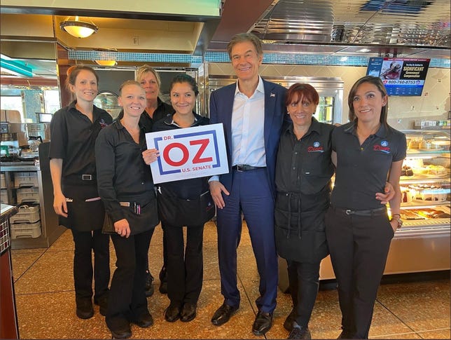 Oz stands with a group of workers at Capitol Diner in Pennsylvania. A woman in the group holds up a campaign sign.