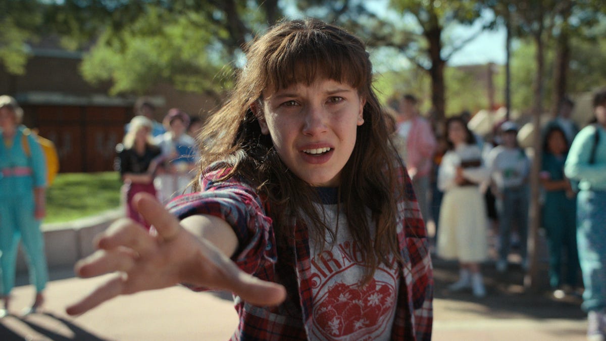 Stranger Things character Eleven stars directly into camera with her arm outstretched toward it