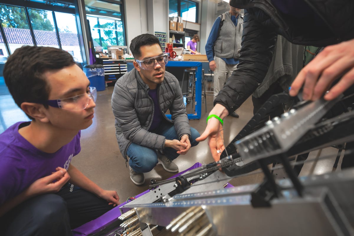 Nate Scher and team mentor Michael Abbott inspect the drive train for the robot's telescope boom which will be used to place point-scoring cones and cubes into the goals.