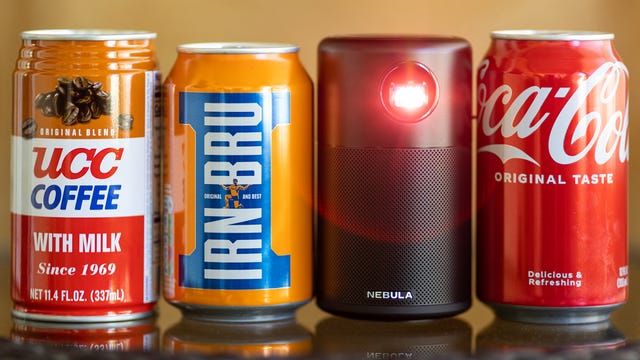 The Anker Nebula Capsule projector beside three soft drink cans