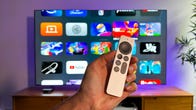 Apple TV remote held up in front of a TV showing various apps