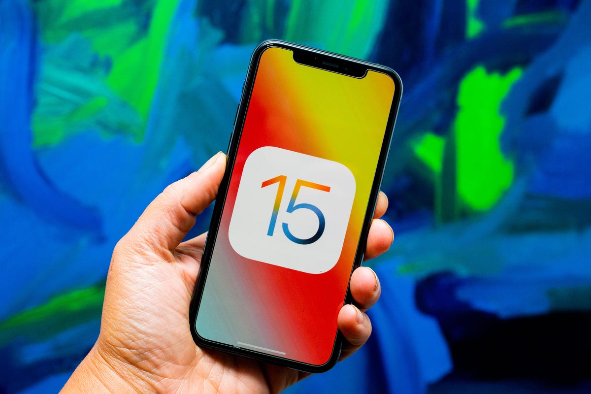 Hand holding an iPhone with iOS 15 logo on the screen