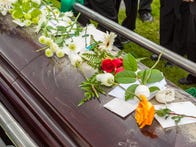 <p>Flowers and cards from loved ones on casket as it is lowered into ground at burial at cemetery.</p>