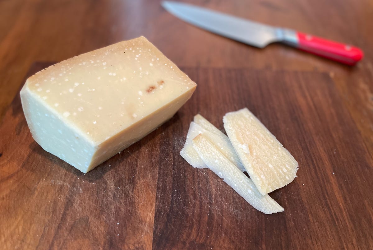 block of cheese on cutting board sliced with knife in background