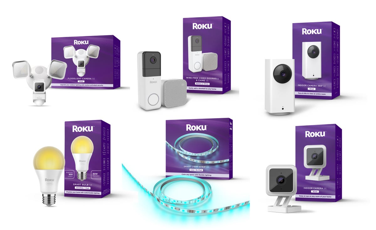 An assortment of six new Roku-branded smart home devices sitting on display beside their packaging. There's an outdoor floodlight camera, a video doorbell and chime, a 360-degree panning camera, a smart bulb, a color-changing smart light strip, and a standard indoor camera.