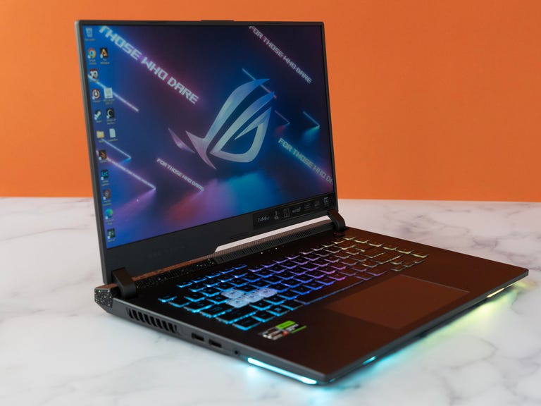 The ROG Strix G15 open and angled to your right, with the RGB illumination on the keyboard and underglow, default ROG wallpaper on a white marbled surface against an orange background